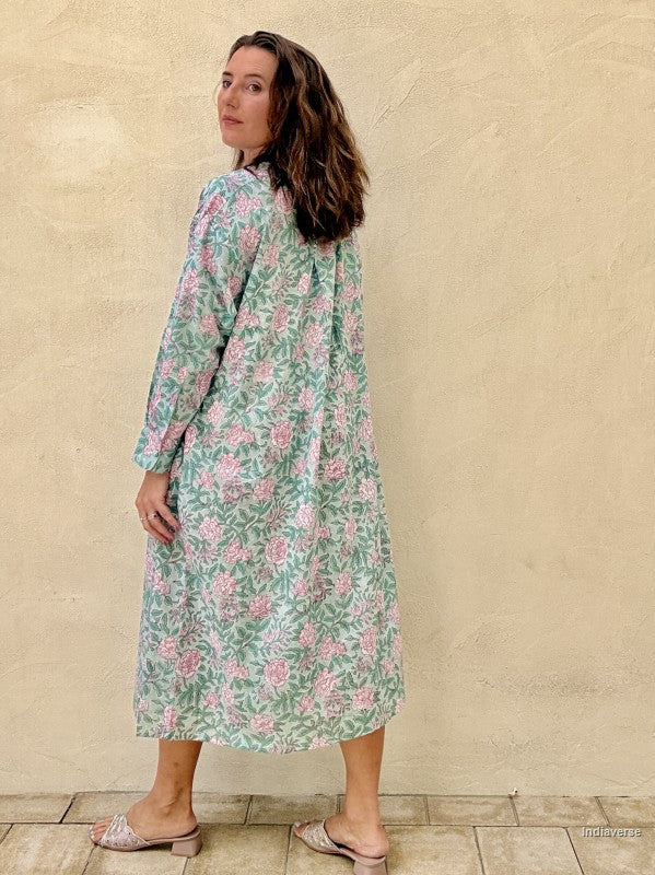 A woman wearing a long-sleeve midi dress with a green and pink floral pattern, standing against a textured beige wall.