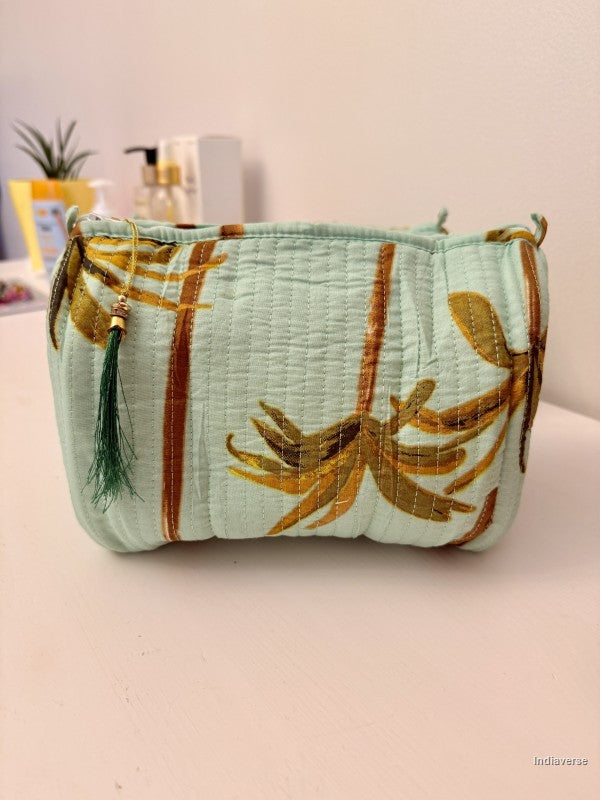A light mint green quilted cosmetic pouch featuring a gold and brown bamboo pattern, with a dark green tassel charm, resting on a light pink surface | Turquoise Palm