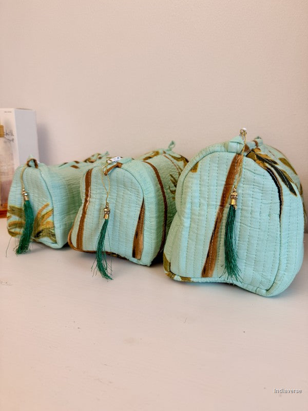Three small quilted cosmetic pouches in a light mint green fabric with gold-toned leaf patterns, brown zipper trims, and green tassels, arranged on a light surface against a pale background | Turquoise Palm