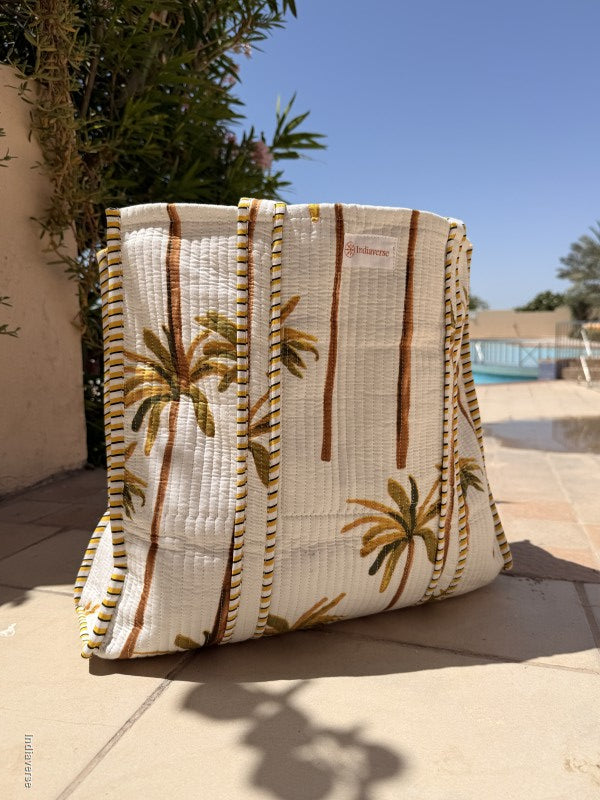 Textile with palm tree design held by a person against a blue sky and building.