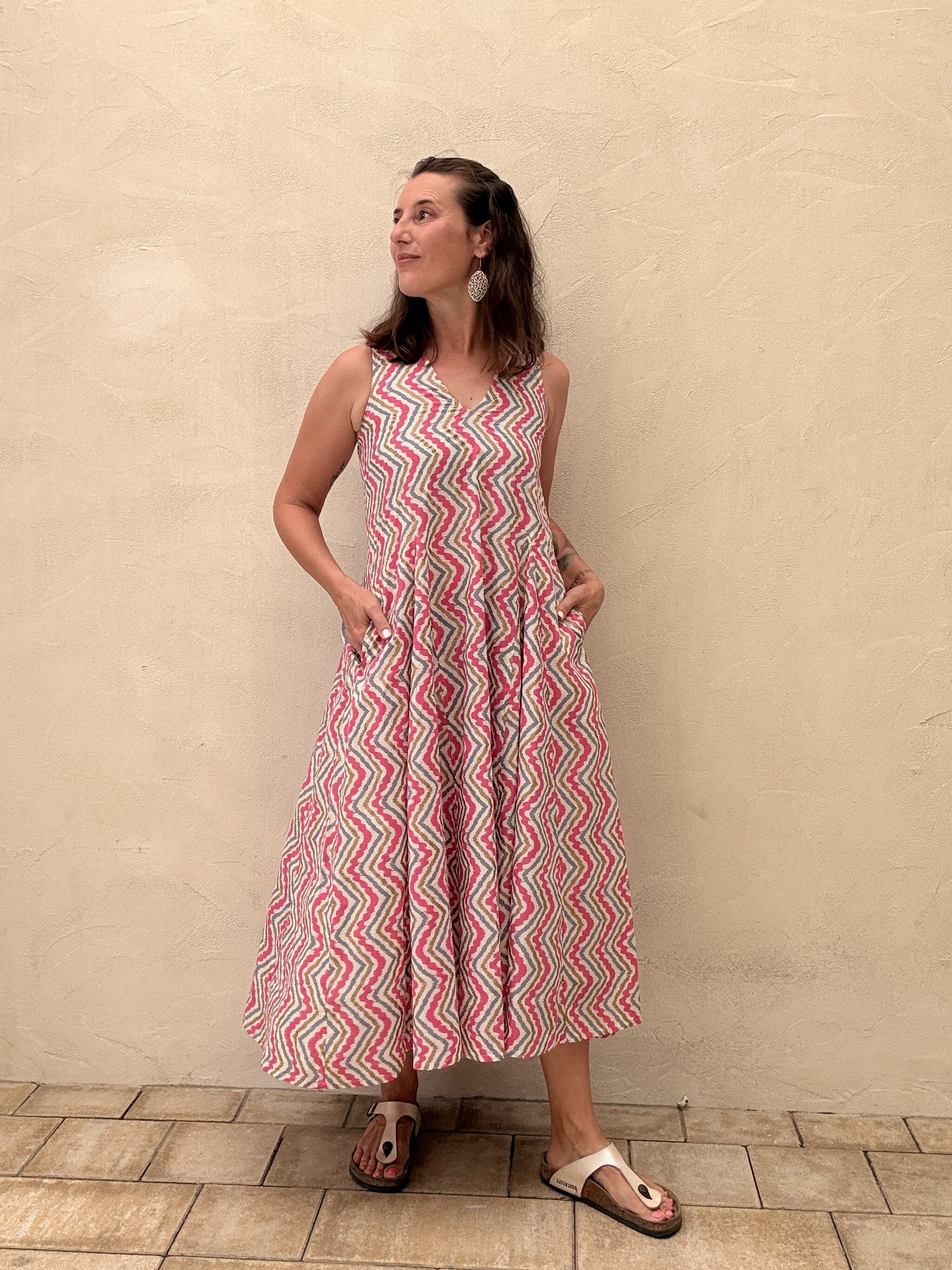 Woman wearing a red and white patterned dress standing against a beige wall.