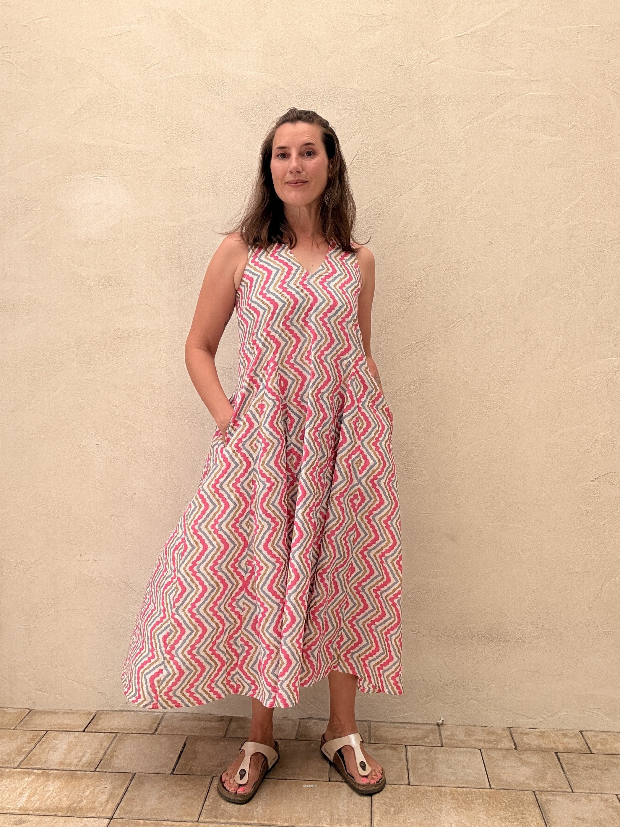 Woman wearing a red and white patterned dress standing against a beige wall.