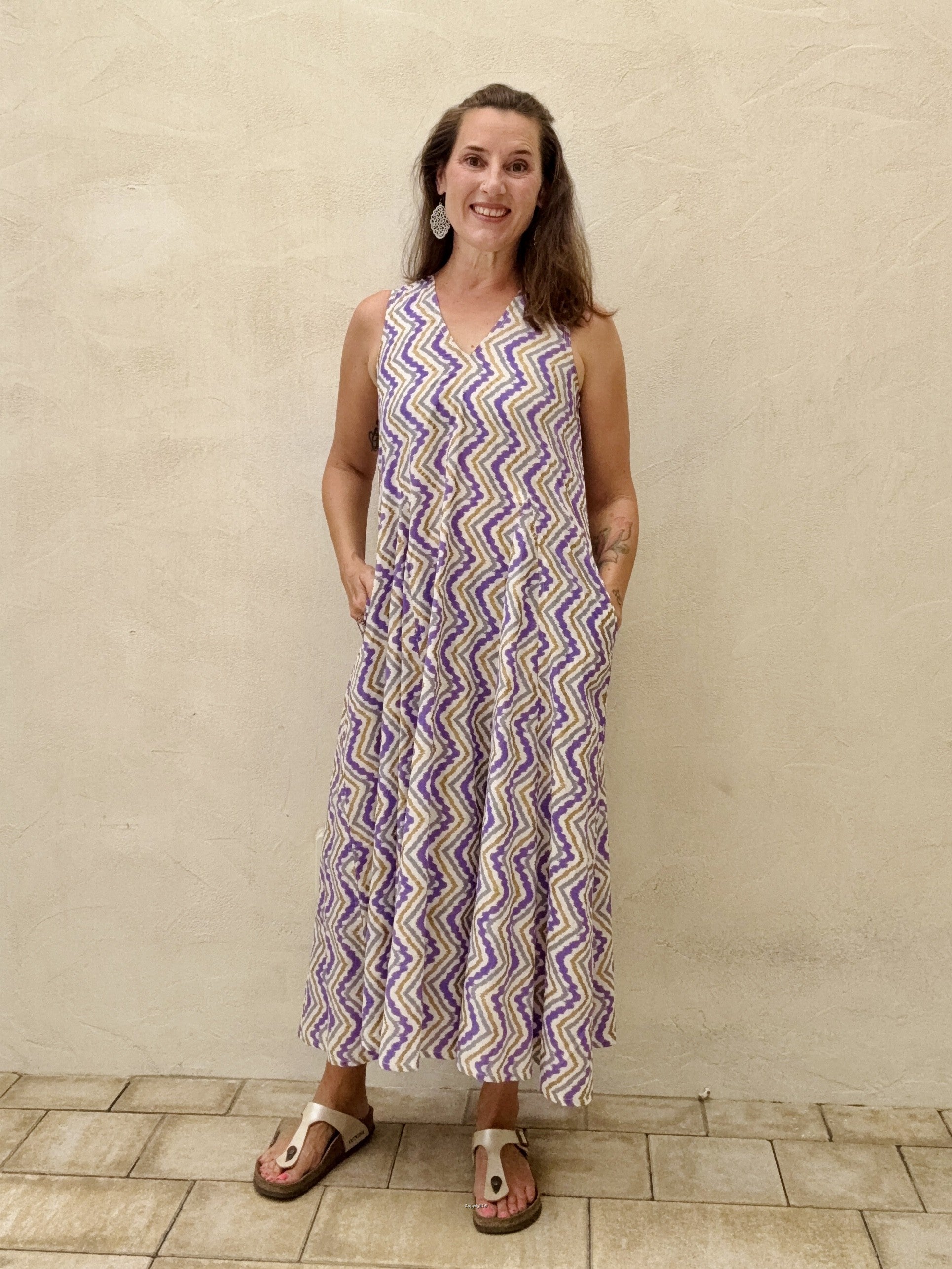 Woman wearing a sleeveless, patterned dress standing against a beige wall.
