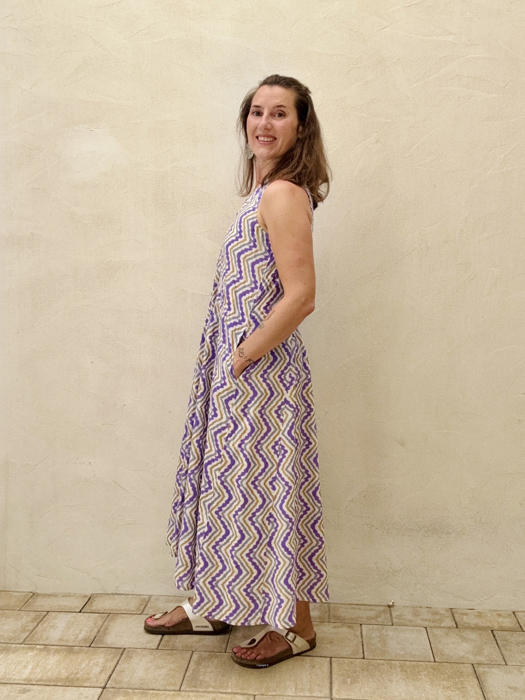 Woman wearing a purple and white patterned dress standing against a beige wall.