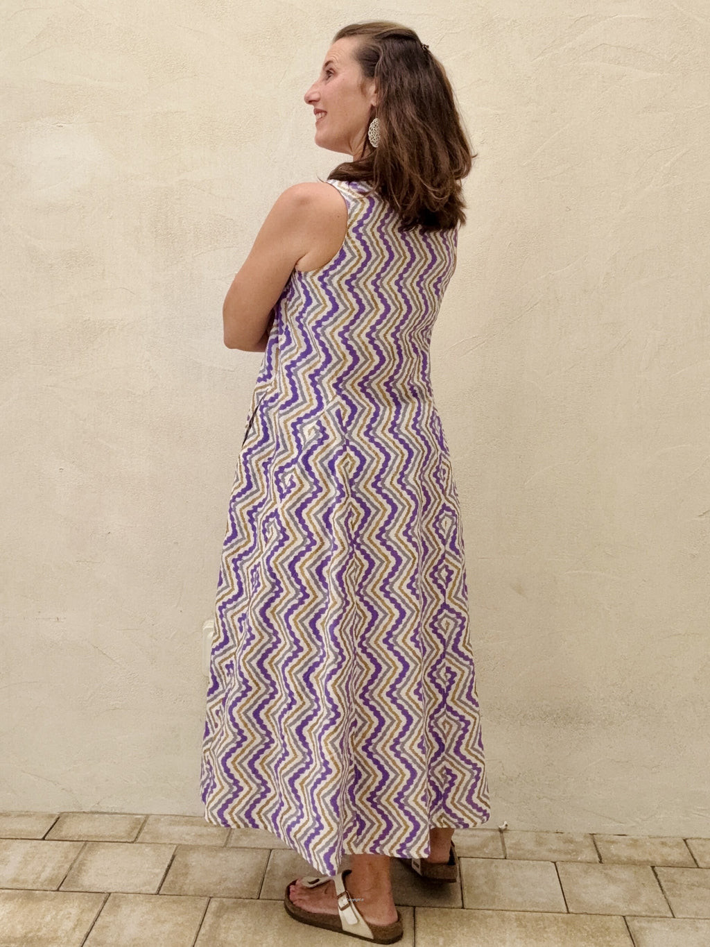 Woman wearing a patterned dress standing against a beige wall.