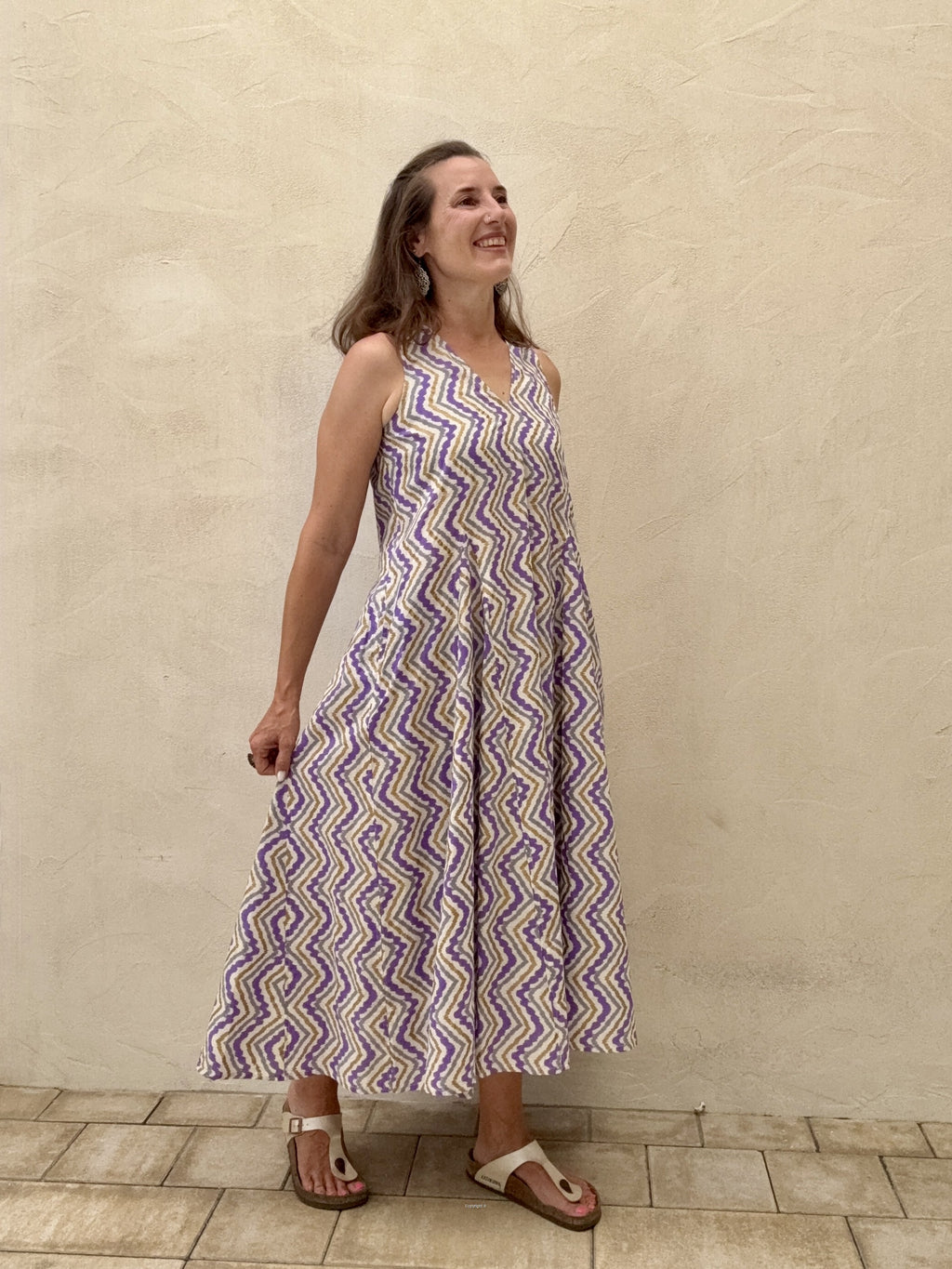 Woman wearing a purple and white zigzag patterned dress standing against a beige wall.