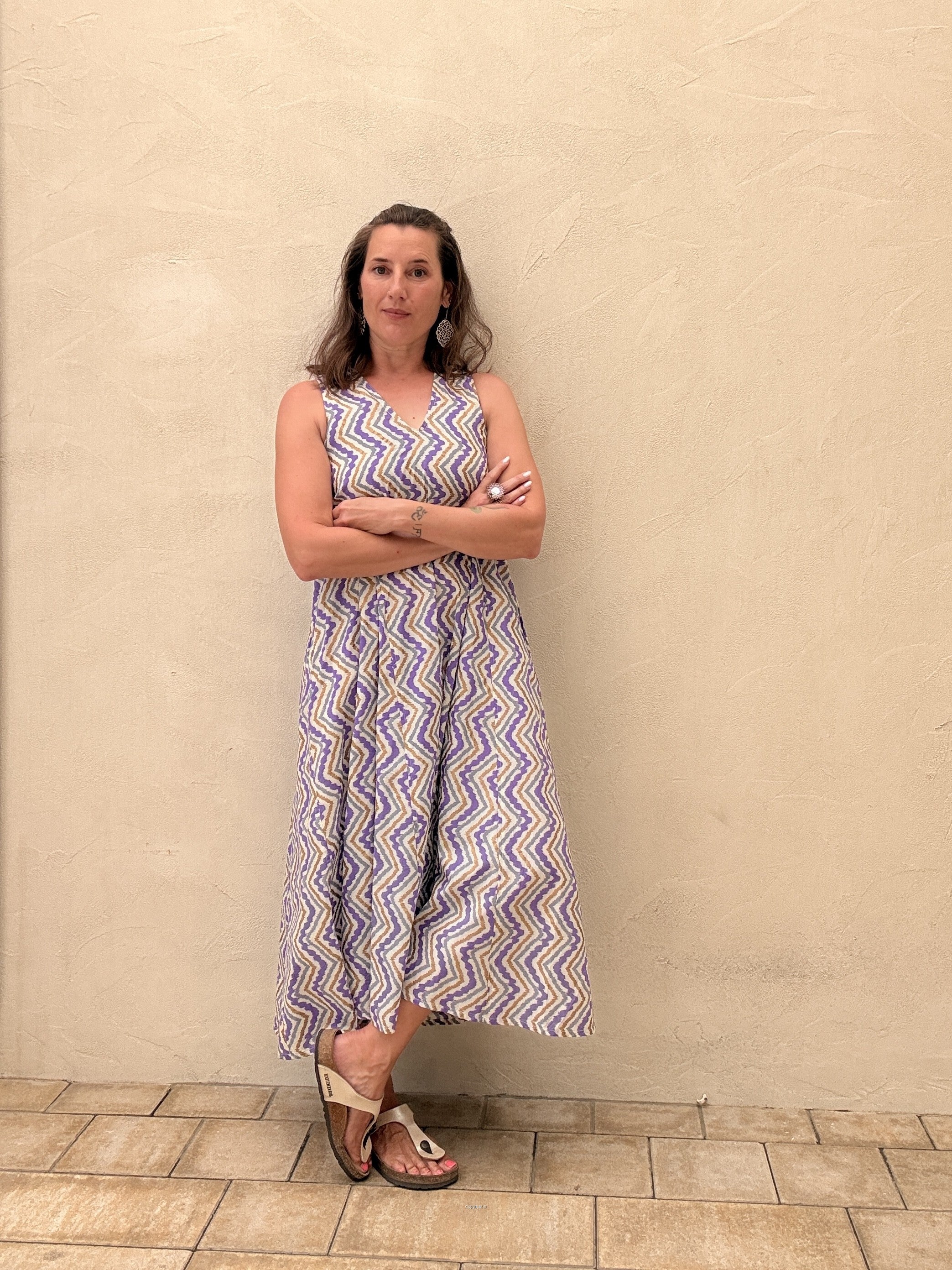 Woman wearing a sleeveless dress with a zigzag pattern against a beige wall.