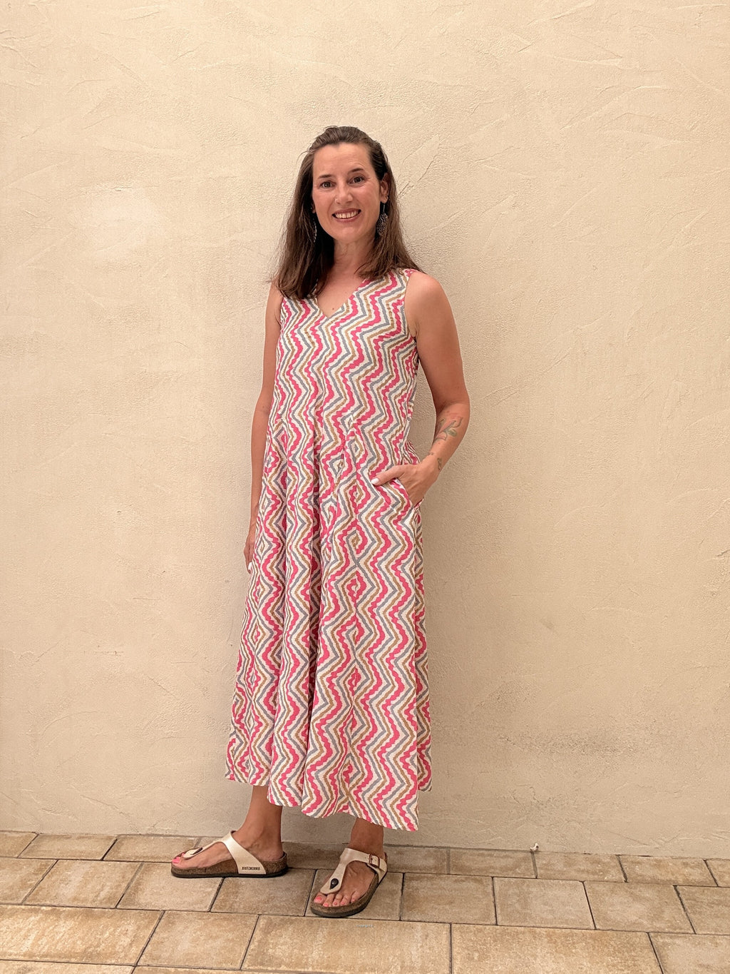 Woman wearing a pink and white patterned dress standing against a beige wall.