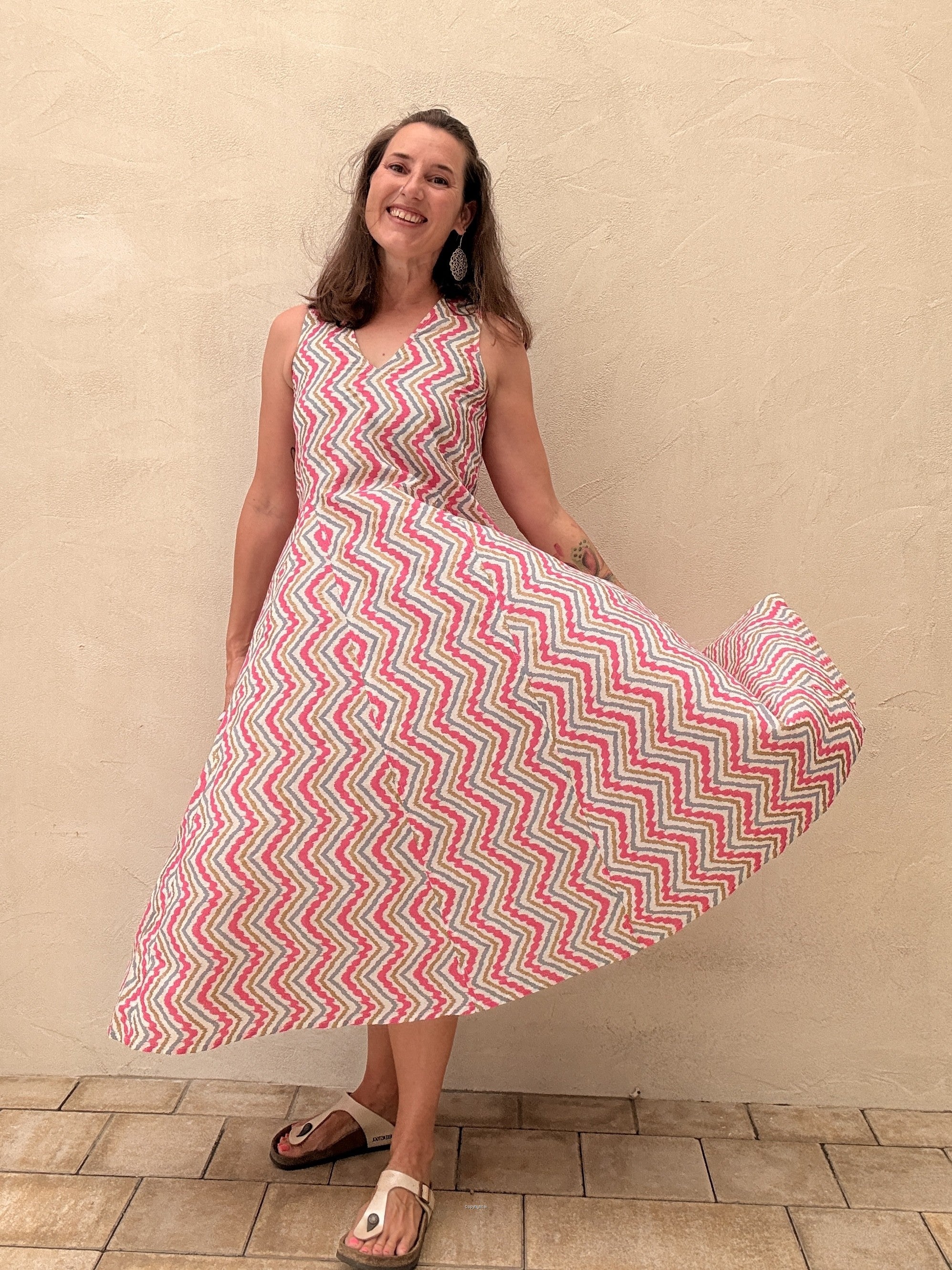 Woman wearing a pink and white zigzag patterned dress against a beige wall.