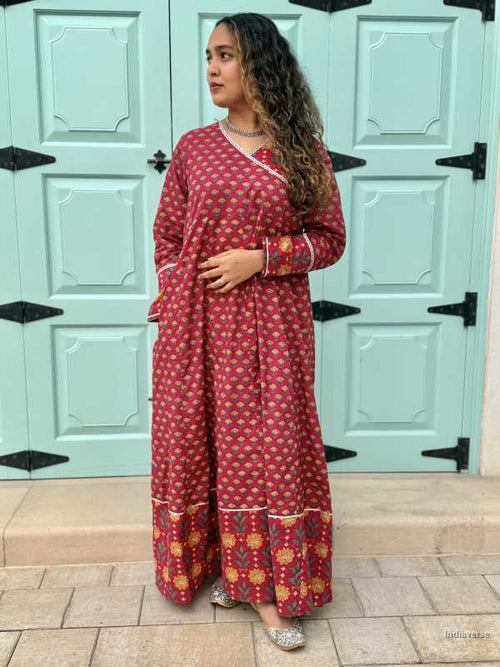 Woman wearing a full length ethnic festive wrap dress with silver border around the neckline and arms and floral trim border in front of light blue colored door