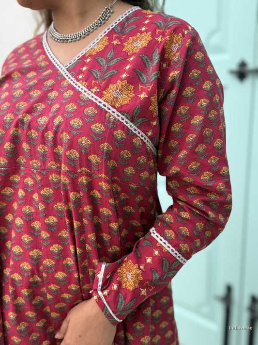 Woman wearing a full length ethnic festive wrap dress with silver border around the neckline and arms and floral trim border in front of light blue colored door