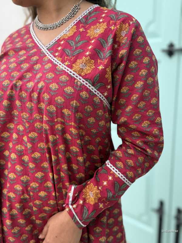 Woman wearing a full length ethnic festive wrap dress with silver border around the neckline and arms and floral trim border in front of light blue colored door