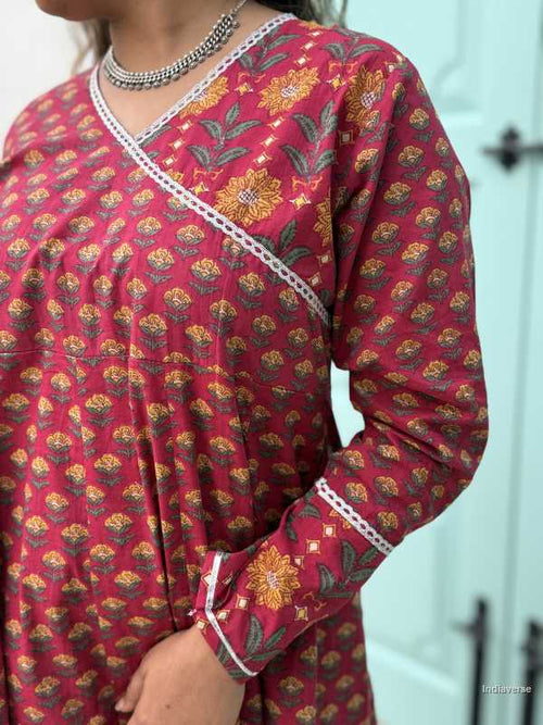 Woman wearing a full length ethnic festive wrap dress with silver border around the neckline and arms and floral trim border in front of light blue colored door