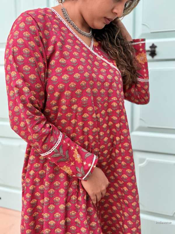 Woman wearing a full length ethnic festive wrap dress with silver border around the neckline and arms and floral trim border in front of light blue colored door