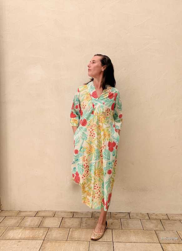 Woman wearing a colorful floral dress against a beige wall.