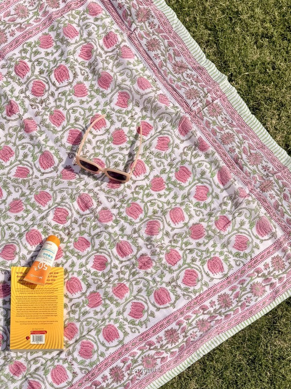 Patterned blanket with sunglasses and a book on grass