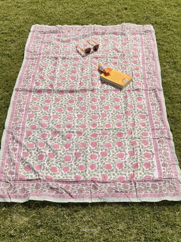 Floral-patterned blanket on grass with sunglasses and a book.
