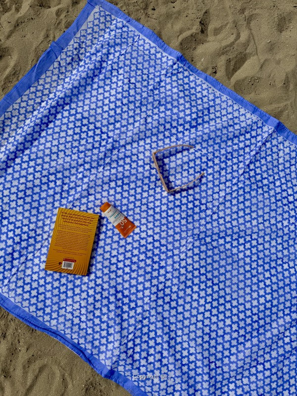 Blue patterned towel on sand with a small bottle and packaging.