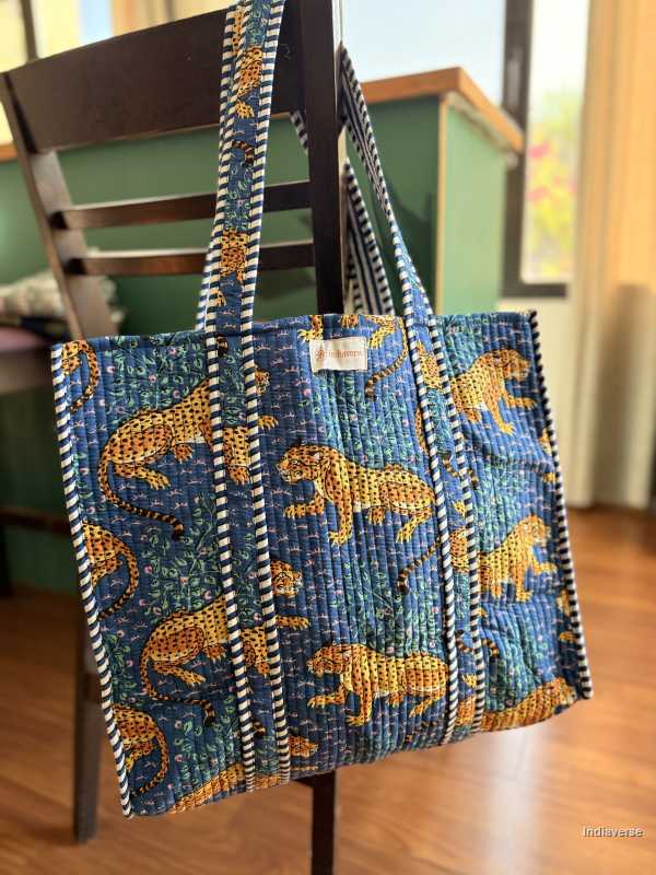 Blue tote bag with orange animal pattern hanging on a chair indoors.