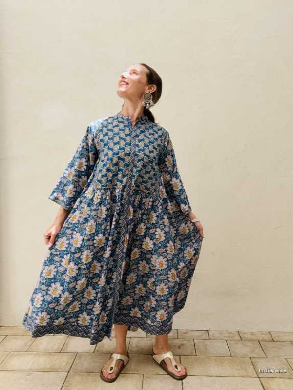 Woman wearing a blue floral dress against a beige wall.