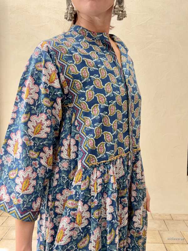 woman standing in front of a beige wall wearing a blue midi size cotton dress with floral and paisley print