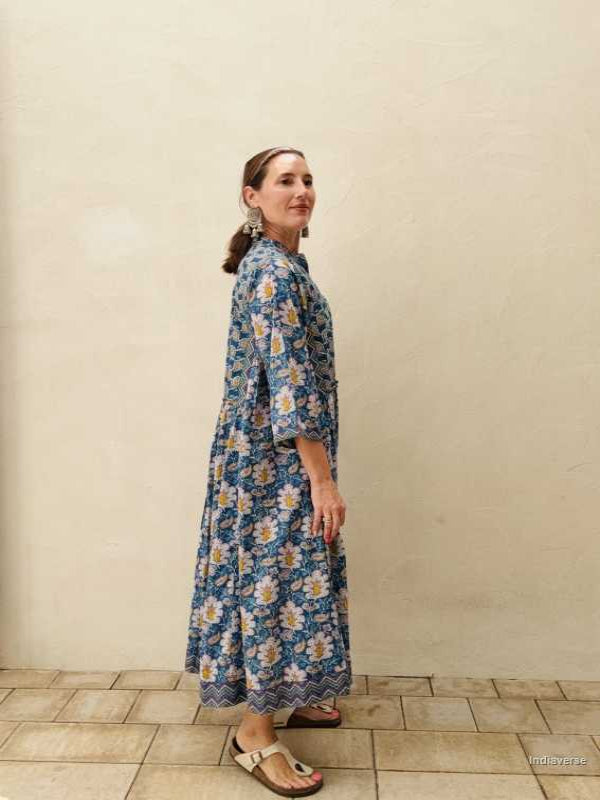 woman standing in front of a beige wall wearing a blue midi size cotton dress with floral and paisley print