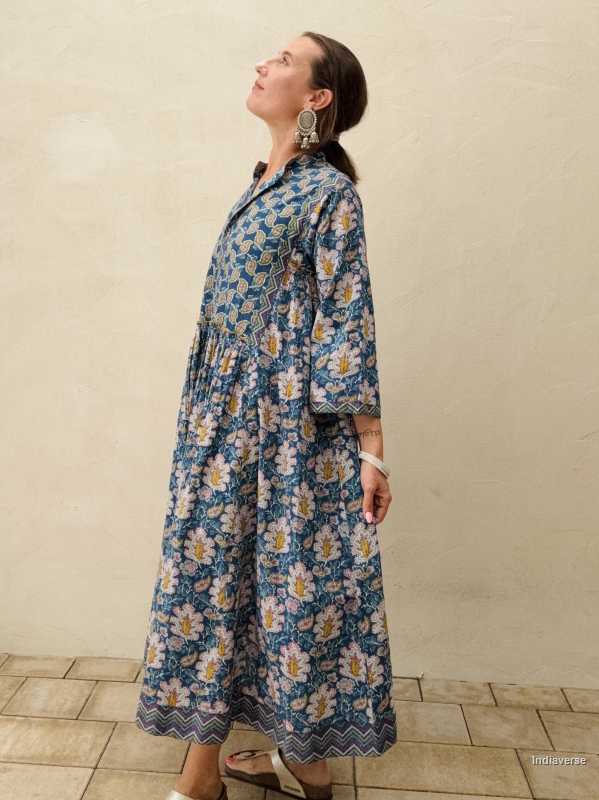 woman standing in front of a beige wall wearing a blue midi size cotton dress with floral and paisley print