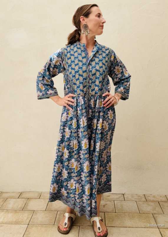 woman standing in front of a beige wall wearing a blue midi size cotton dress with floral and paisley print