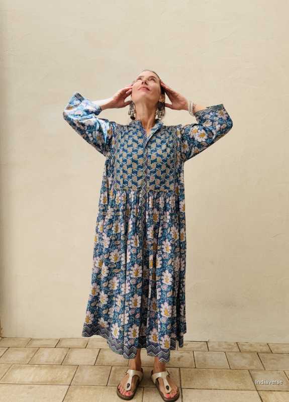 woman standing in front of a beige wall wearing a blue midi size cotton dress with floral and paisley print
