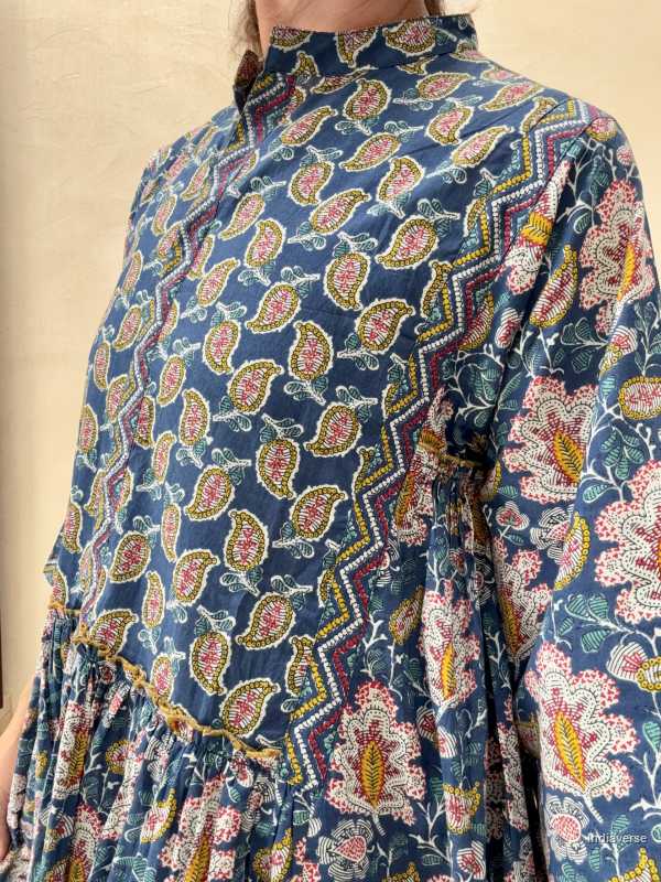 woman standing in front of a beige wall wearing a blue midi size cotton dress with floral and paisley print