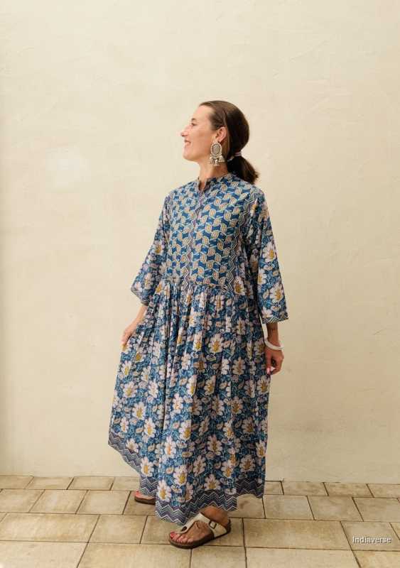 woman standing in front of a beige wall wearing a blue midi size cotton dress with floral and paisley print