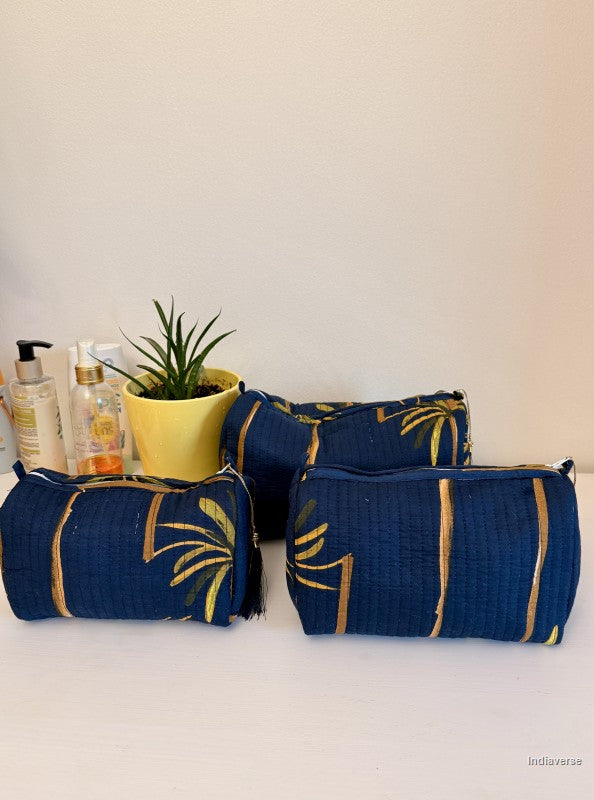 Set of blue and gold cosmetic bags on a white surface with a plant and bottles in the background | Blue Palm