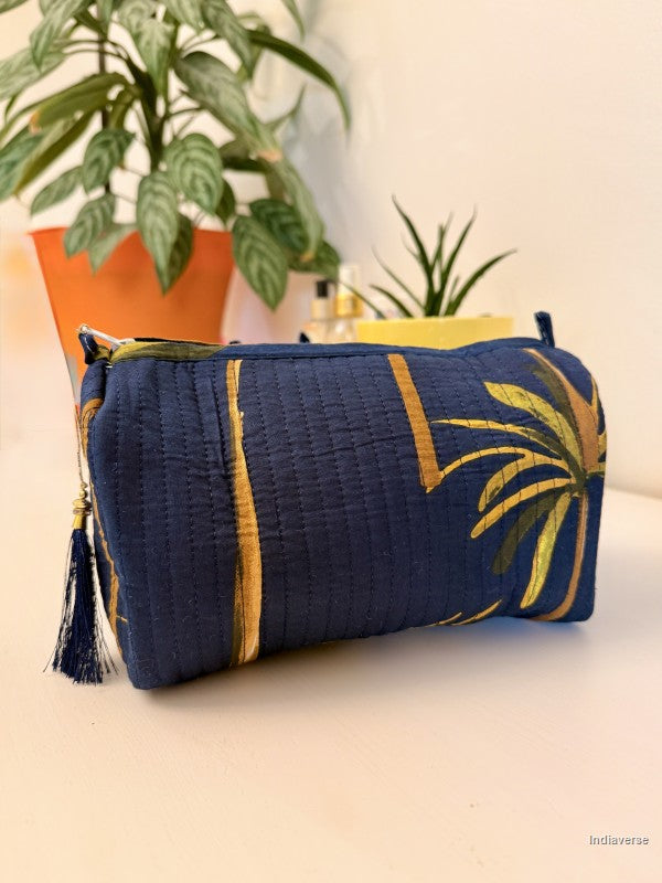 Blue pouch with gold accents and leaf patterns on a white surface with plants in the background | Blue Palm
