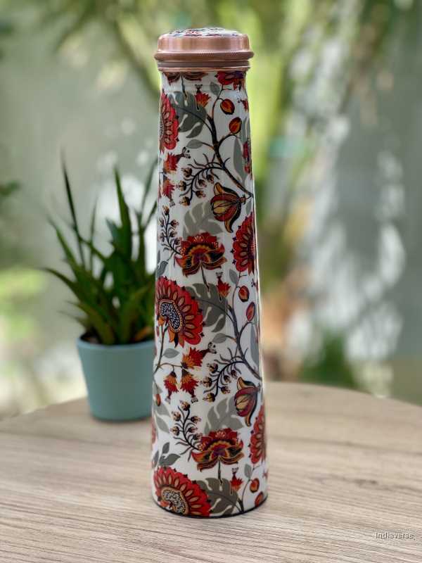 Tower shaped copper bottle with enameled red and grey floral design on a white base for carrying water with a capacity of 750 ml 