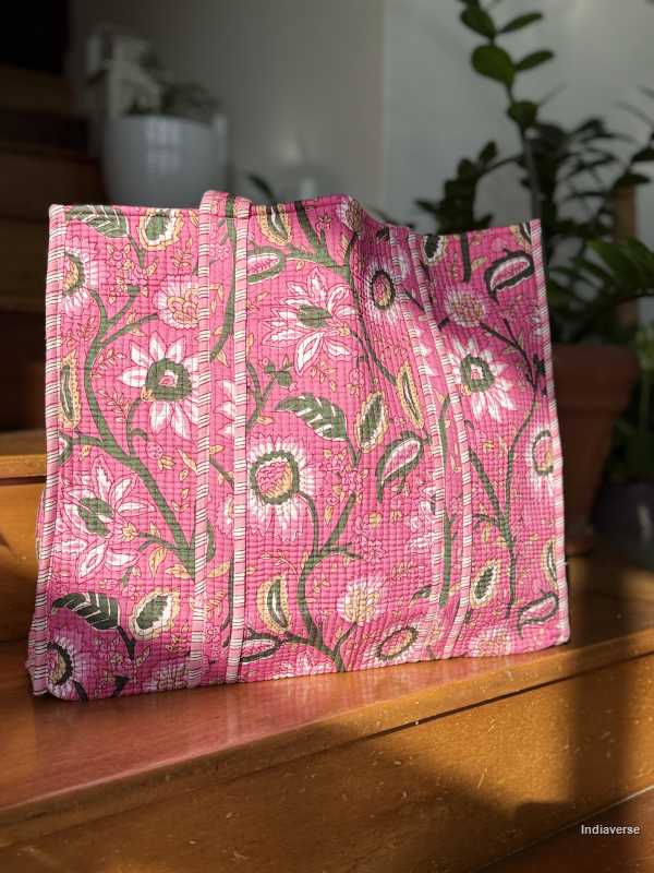 Pink floral fabric tote bag on a wooden surface with plants in the background