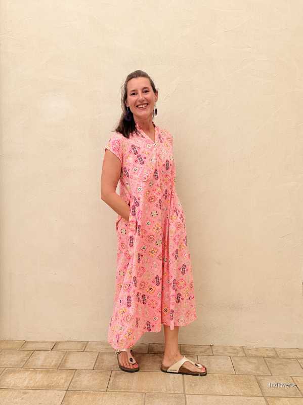 Woman wearing a pink floral dress standing against a beige wall.