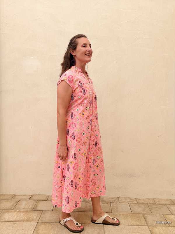 Woman wearing a pink floral dress standing against a beige wall.