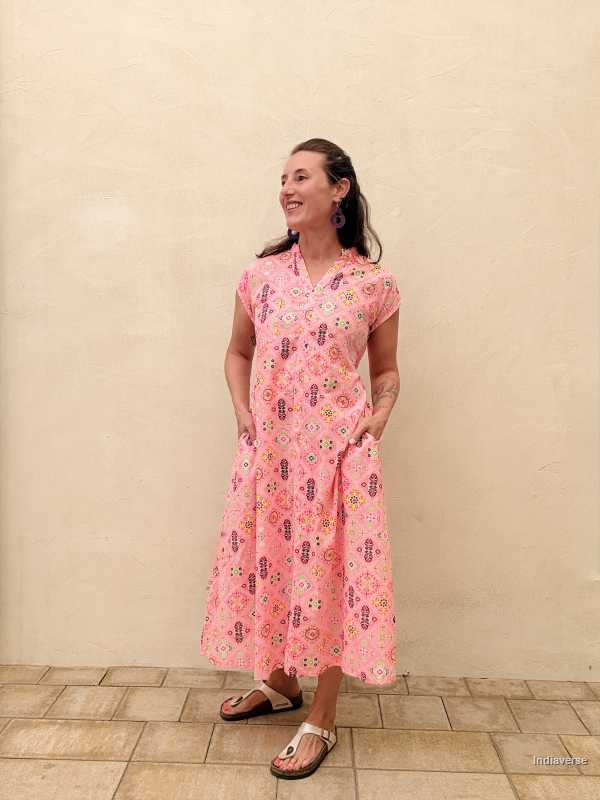 Woman wearing a pink floral dress standing against a beige wall.
