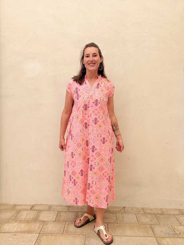 Woman wearing a pink floral dress standing against a beige wall.