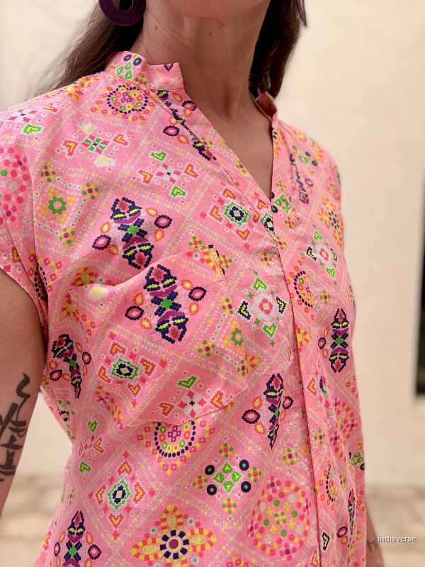Person wearing a pink dress with chest pocket and colorful patterns on a blurred background