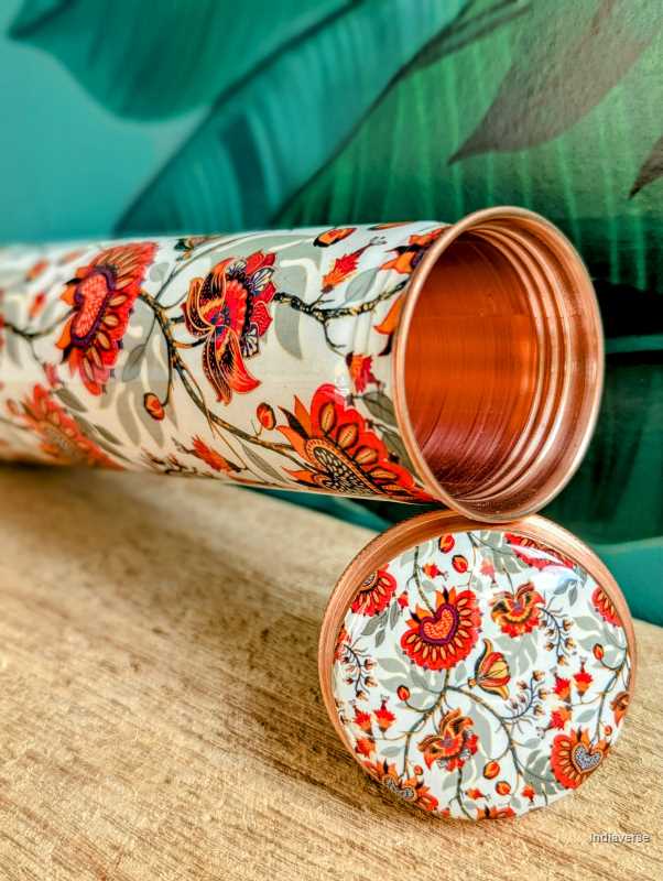 Tower shaped copper bottle with enameled red and grey floral design on a white base for carrying water with a capacity of 700 ml 