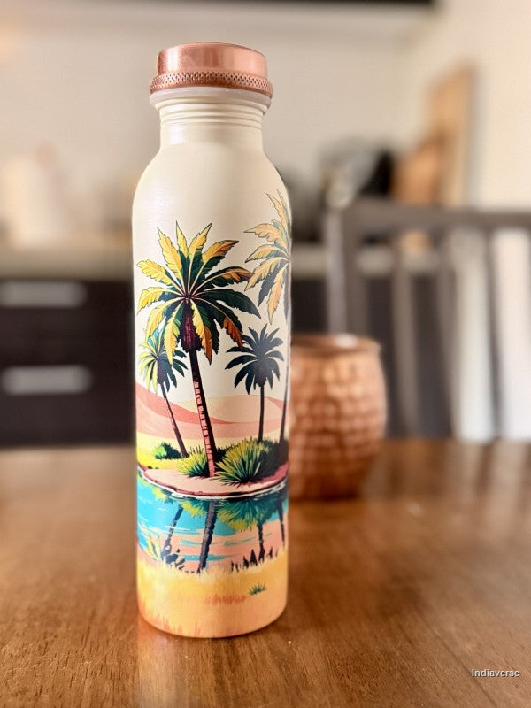 copper water bottle for drinking water with colorful palm tree oasis design in a desert on beige background standing on a brown table with a copper cup in the background
