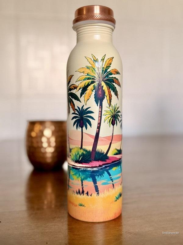 copper water bottle for drinking water with colorful palm tree oasis design in a desert on beige background standing on a brown table with a copper cup in the background
