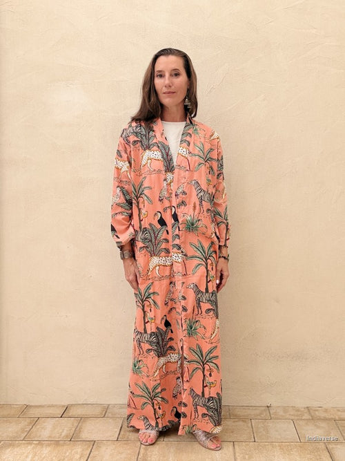Woman wearing a long, patterned dress against a beige wall.