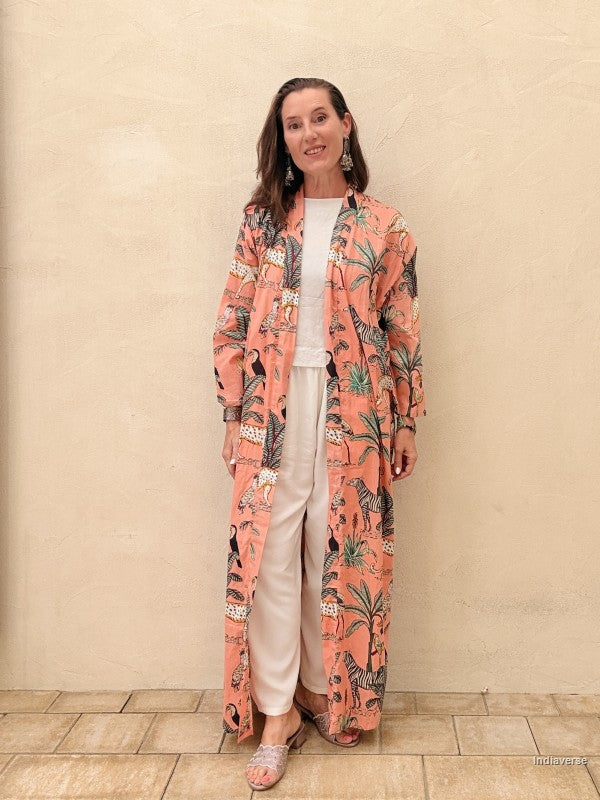 Woman wearing a long, patterned pink coat against a beige wall.