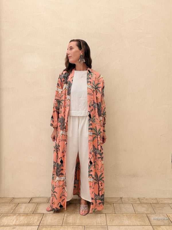 Woman wearing a long floral coat over a white outfit against a beige wall.