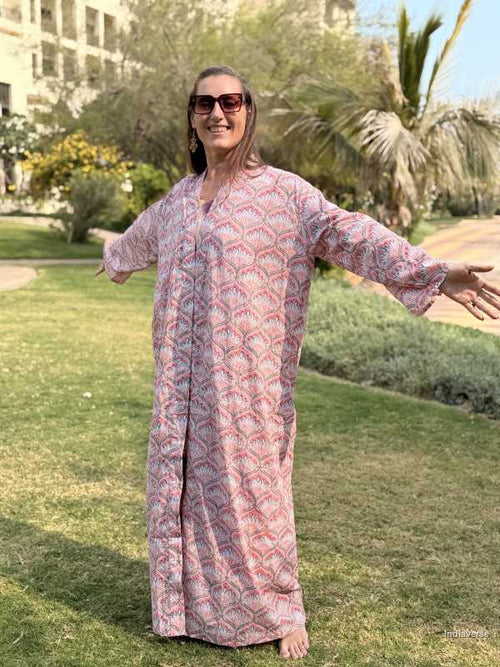 Woman in a patterned dress standing outdoors with greenery and palm trees in the background
