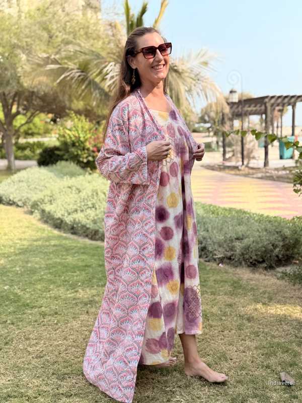 Woman wearing a long, patterned dress standing outdoors with greenery in the background