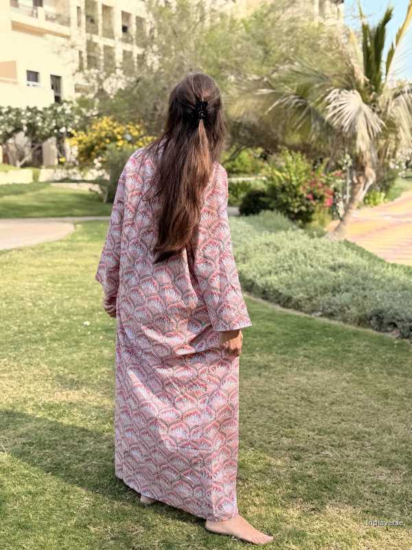 Person wearing a pink patterned dress standing on grass with a garden and building in the background
