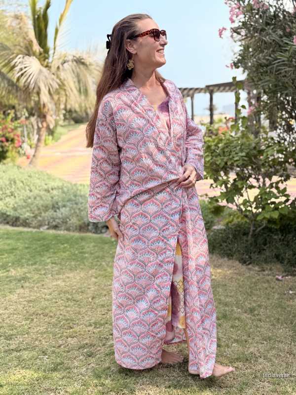 Woman in a pink patterned outfit standing outdoors with greenery and a clear sky.